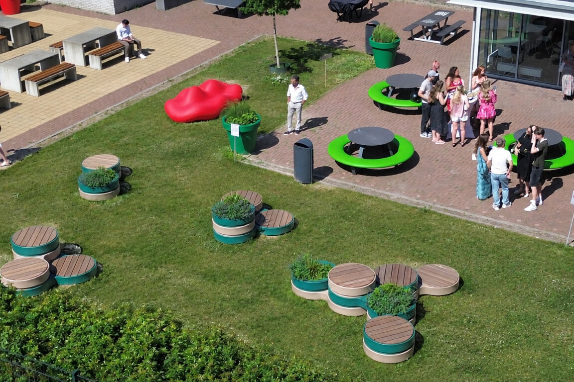 Vernieuwd schoolplein van ROC Mondriaan in Den Haag met kleurrijk meubilair, modulaire zitplekken, schommelbank, sport- en spelelementen en groene accenten, waar leerlingen samenkomen, ontspannen en bewegen.